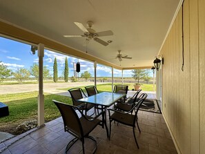A covered patio with a table and chairs, a ceiling fan, and a view of the surrounding landscape. - The Napoleon (Fort Stockton)