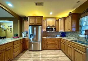 A kitchen with wooden cabinets, a stainless steel refrigerator, a microwave, and a granite countertop. - The Napoleon (Fort Stockton)