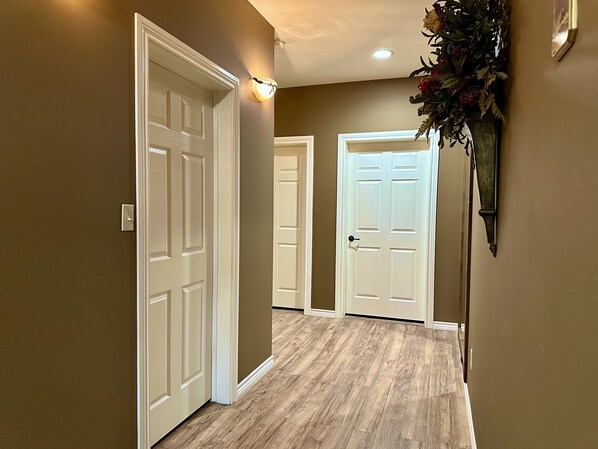A hallway with wooden flooring, white doors, and a wall-mounted light fixture. - The Napoleon (Fort Stockton)