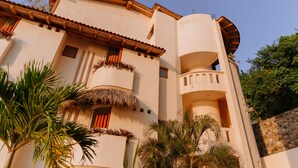 A multi-story building with a curved facade, balconies with thatched roofs, and a stone wall. - Pacífica Grand Zihuatanejo (Zihuatanejo)