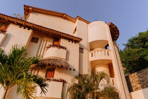 Un edificio de varios pisos con fachada curva, balcones con techos de paja y una pared de piedra.