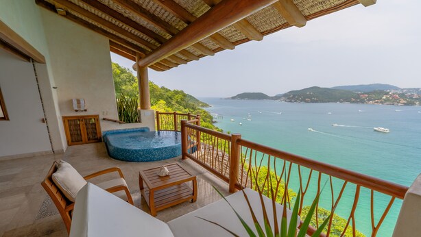 A balcony with a view of the sea, a hot tub, and a wooden table with chairs. - Pacífica Grand Zihuatanejo (Zihuatanejo)