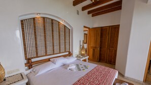 A neatly made bed with a white and red patterned bedspread, a wooden headboard, and a bedside table with a lamp and a vase. - Pacífica Grand Zihuatanejo (Zihuatanejo)