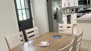 A modern kitchen with white cabinets, stainless steel appliances, and a wooden dining table with chairs.