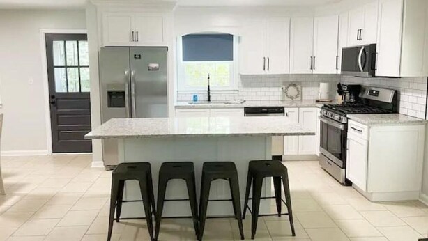 A modern kitchen with white cabinets, a central island with bar stools, a refrigerator, microwave, stove, and dishwasher.
