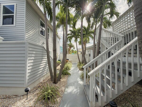 A pathway flanked by white buildings and palm trees, leading to a white staircase.