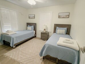 A bedroom with two beds, a nightstand, a lamp, and a ceiling fan.
