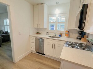A compact kitchen with white cabinets, a dishwasher, a sink, and a stove.