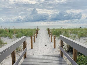 A wooden boardwalk leading to a beach with sand and grassy dunes.