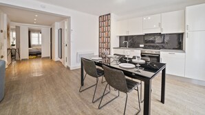 Una cocina moderna con armarios blancos, encimera negra y comedor con mesa y sillas de vidrio.