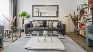Una sala de estar moderna con un sofá gris, una mesa de centro de vidrio y una estantería llena de libros.