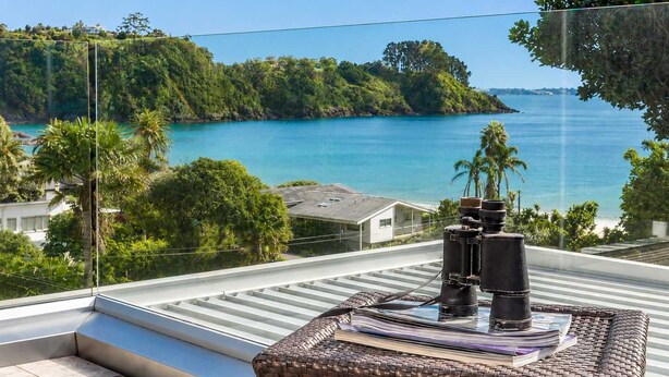 A balcony with a view of a turquoise sea and green hills.