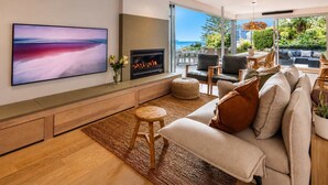 A modern living room with a flat-screen TV, a fireplace, a sofa, and a view of the outdoors.