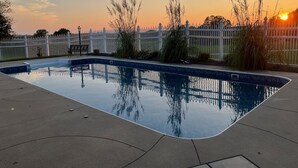 Une piscine entourée d’une clôture blanche et de plantes.