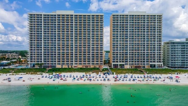 Um hotel à beira-mar com vários edifícios altos, uma praia arenosa e águas turquesa cristalinas.