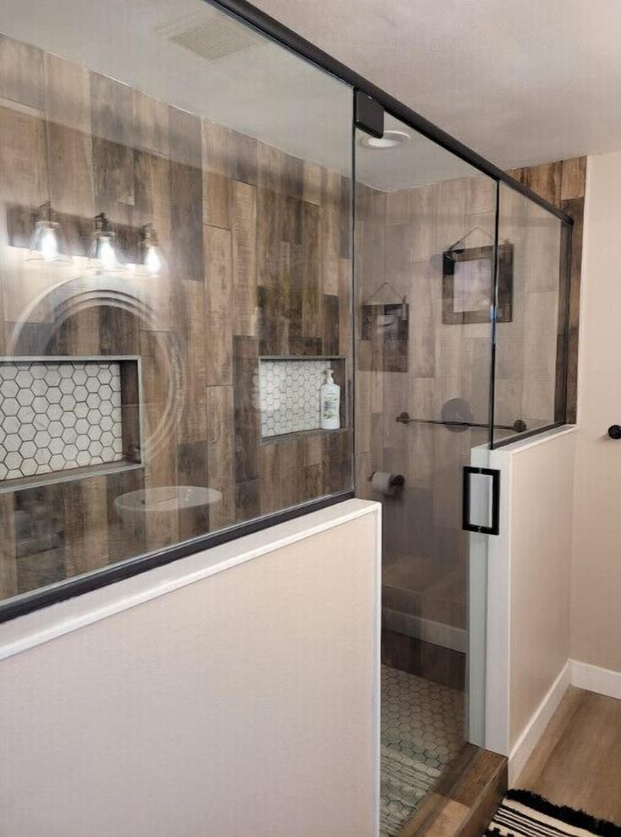 Une salle de bain moderne dotée d’une douche à parois de verre, de panneaux muraux en bois et d’un pare-splash en carreaux hexagonaux.