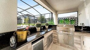 A modern kitchen with a built-in grill, a wine glass, and potted plants.