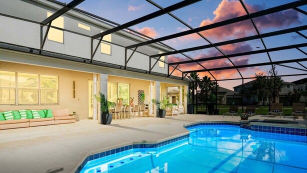 A swimming pool with a glass ceiling, a sofa, and a dining area with chairs and plants.