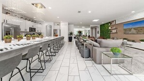 A modern kitchen with a long island, bar stools, and a dining area with a sofa and coffee table.