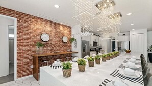 A modern kitchen with a brick wall, stainless steel appliances, and a long dining table with potted plants.