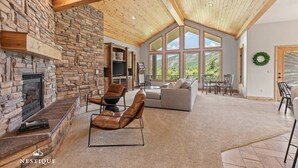 A spacious living area with a stone fireplace, leather recliner, and a large window offering a view of the outdoors. - New to Market Private Weber River Access Stunning Family Retreat (Morgan)