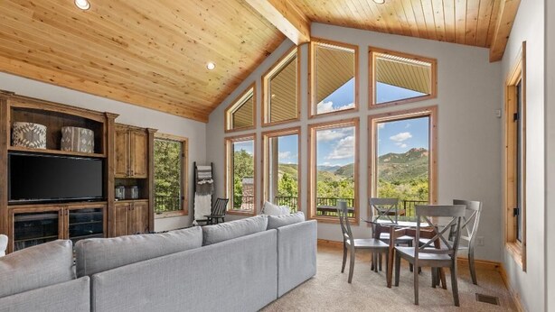 A spacious living room with a large gray sectional sofa, wooden cabinets, a flat-screen TV, and a dining area with a table and chairs. - New to Market Private Weber River Access Stunning Family Retreat (Morgan)