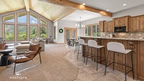 A spacious kitchen with wooden cabinets, a bar area, and large windows offering a view of the outdoors. - New to Market Private Weber River Access Stunning Family Retreat (Morgan)