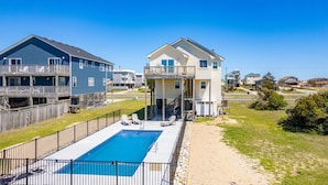A residential area with a swimming pool, a two-story house with a balcony, and a neighboring blue house. - Carolina Sol: Semi-Oceanfront, Private Pool, Close to beach and Outer Banks Fishing Pier (Nags Head)