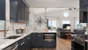 A modern kitchen with dark cabinetry, a central island, and a built-in oven. - Carolina Sol: Semi-Oceanfront, Private Pool, Close to beach and Outer Banks Fishing Pier (Nags Head)