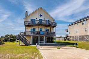 A multi-story building with a balcony, a tennis court, and a sign indicating a coastal vacation rental.