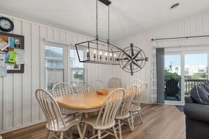 Un comedor con una mesa redonda de madera rodeada por seis sillas, una lámpara colgante y una brújula fijada a la pared.