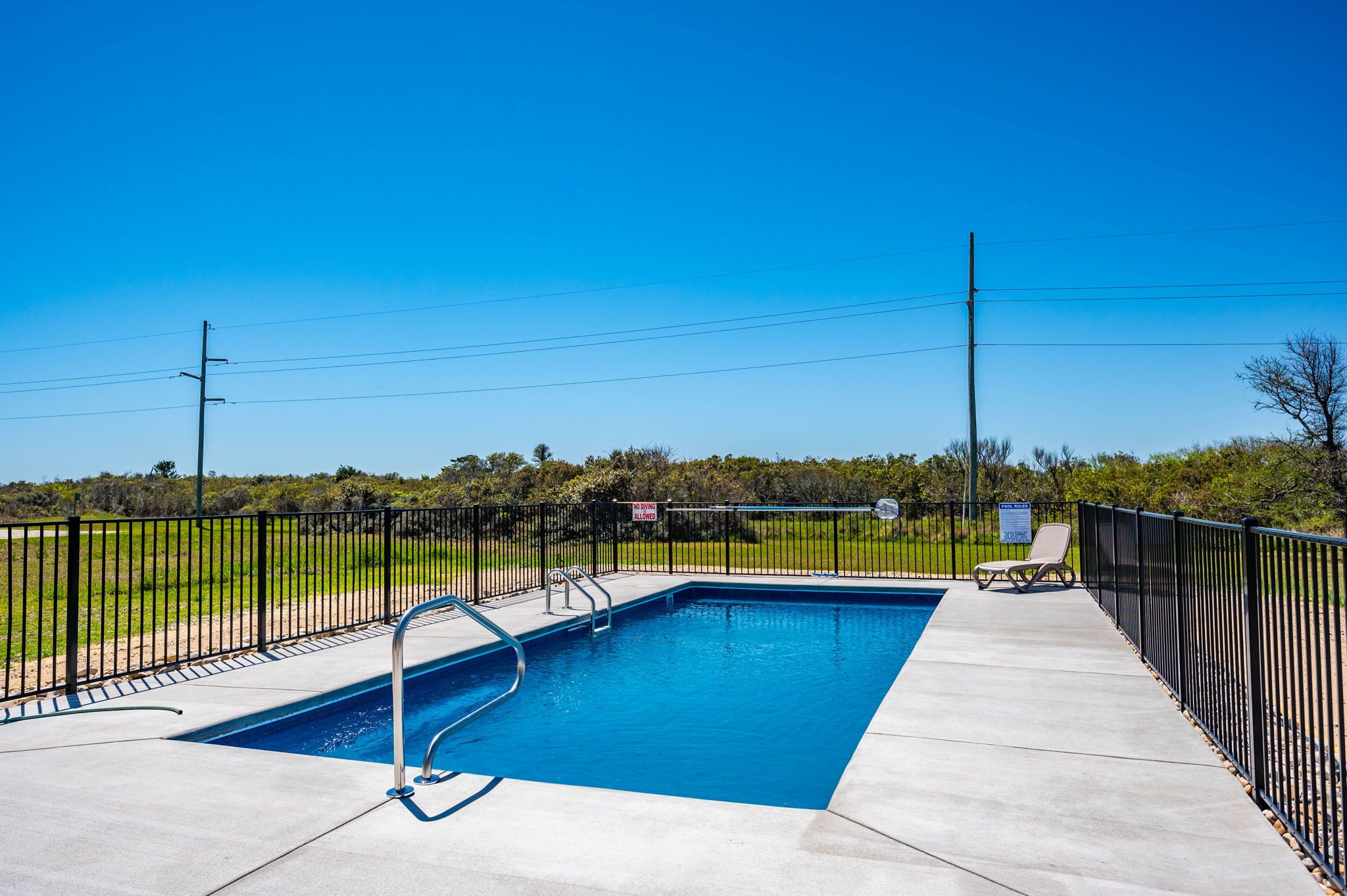 A rectangular swimming pool with a metal ladder, surrounded by a black metal fence, and a clear blue sky in the background.