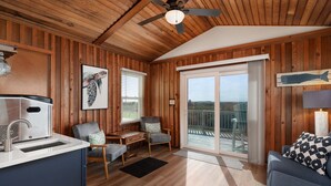 A cabin interior with a kitchenette, seating area, and a balcony with a view. - Carolina Sol: Semi-Oceanfront, Private Pool, Close to beach and Outer Banks Fishing Pier (Nags Head)