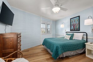 Un dormitorio con cama, escritorio, silla, ventilador de techo y ventana.