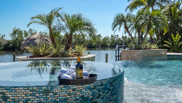 Una piscina con borde de mosaico, una botella de vino y una toalla.