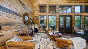 L’intérieur d’une cabane en rondins, avec une grande fenêtre, une cheminée, des meubles en cuir et un plancher en bois.