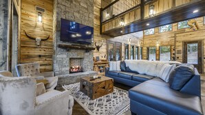 L’intérieur d’une cabane en rondins, avec une cheminée en pierre, un grand canapé bleu et un téléviseur fixé au mur.