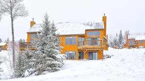 A multi-story wooden building with a balcony, surrounded by snow-covered trees. - Saddleback - Black Gnat Condo #12 (Sandy River Plantation)