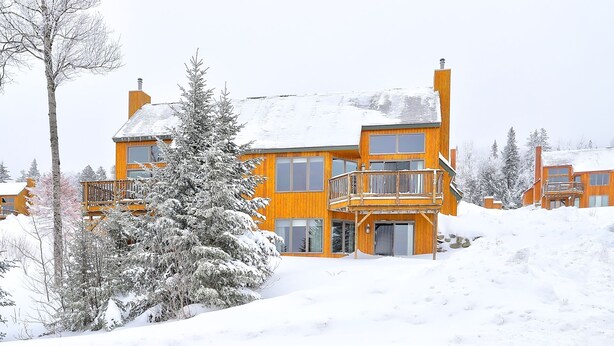 Un edificio de madera de varios pisos con un balcón, rodeado de árboles cubiertos de nieve.