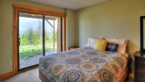 A bedroom with a large bed, a nightstand, and a sliding glass door leading to a balcony with a view of trees and mountains. - Saddleback - Black Gnat Condo #12 (Sandy River Plantation)