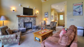 A cozy living room with a stone fireplace, comfortable seating, and a mounted television. - Saddleback - Black Gnat Condo #12 (Sandy River Plantation)