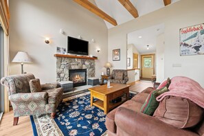 A cozy living room with a stone fireplace, patterned armchairs, a television, and a poster on the wall.