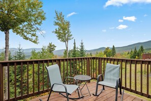 A wooden deck with two rocking chairs and a small table, overlooking a mountainous landscape. - Saddleback - Black Gnat Condo #12 (Sandy River Plantation)