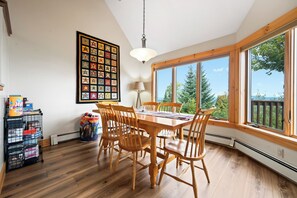 A dining area with a wooden table and chairs, a large window with a view of trees, and a wall-mounted star quilt. - Saddleback - Black Gnat Condo #12 (Sandy River Plantation)