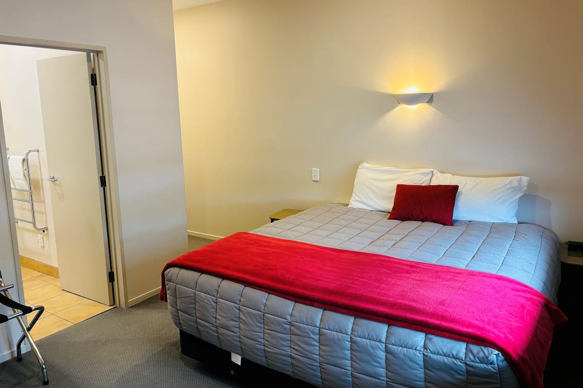 A bedroom with a bed, a red throw blanket, and a wall-mounted light.