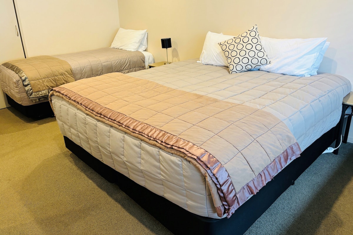 A double bed with a beige quilt and a single bed with a similar quilt.