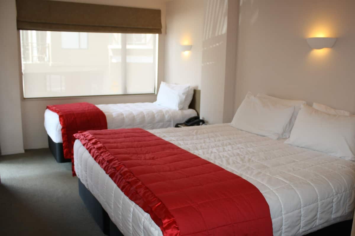 Two beds with red and white bedding, a window with a brown blind, and a wall-mounted light fixture.