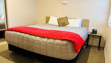 A neatly made bed with a red and beige quilt, a bedside phone, and a wall-mounted light fixture.