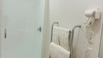 A bathroom with a glass shower enclosure, a towel rack with a towel, a hairdryer, and a sink.
