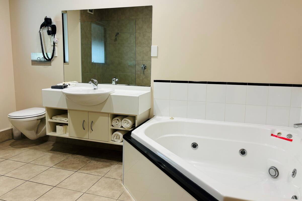 A modern bathroom with a bathtub, two sinks, a toilet, and a hairdryer on the wall.